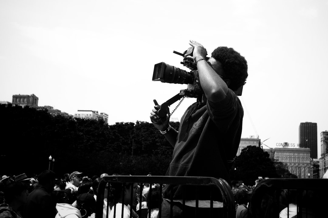 A person films with a camera against a city skyline.